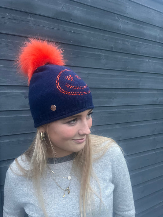 Navy cashmere plain knit beanie with an orange smiley embellishment & faux fur pom